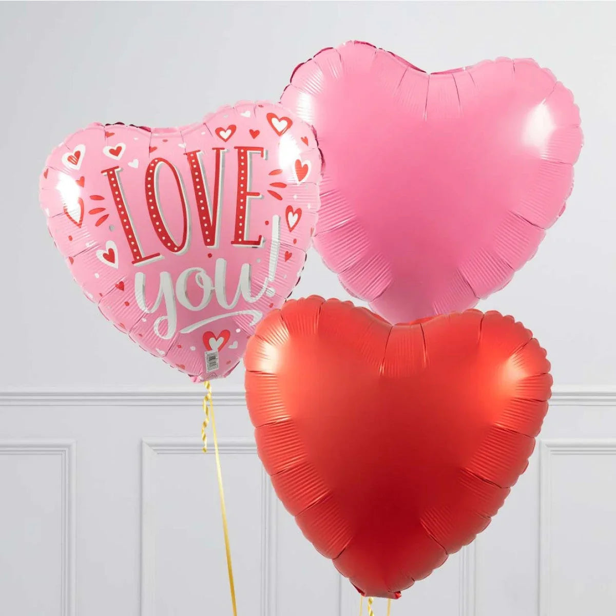 Three heart-shaped foil balloons in pink and red, one pink balloon says Love You with heart patterns