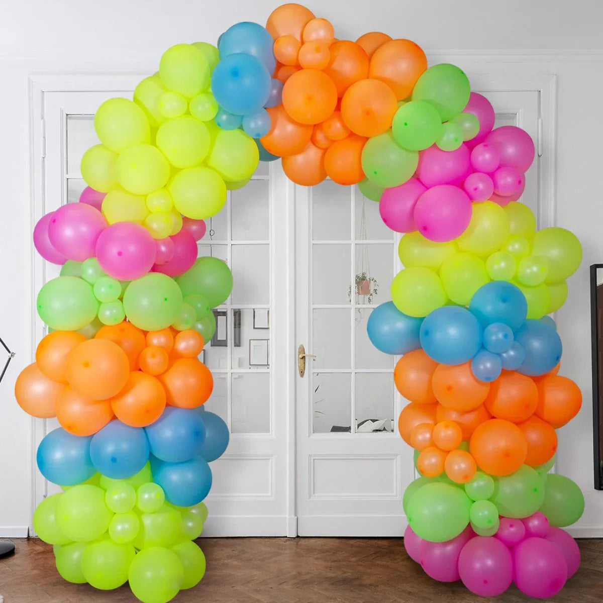 Colorful balloon arch with neon pink, orange, green, blue, and yellow balloons in front of white double doors
