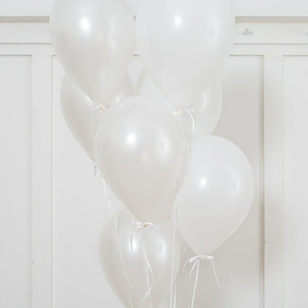 Cluster of pearl white helium latex balloons tied with white ribbons against white panel wall
