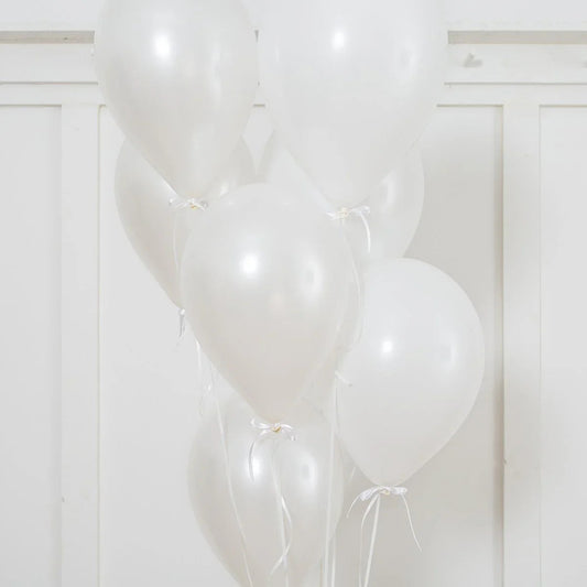 Cluster of pearl white helium latex balloons tied with white ribbons against white panel wall