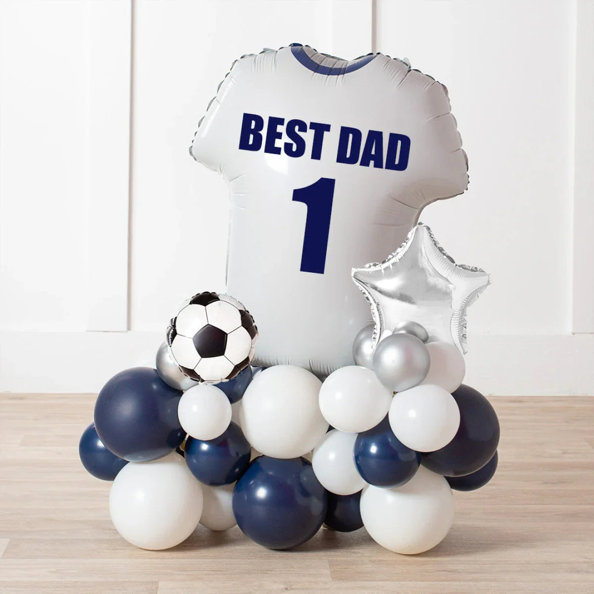 White balloon shaped like a football jersey with Best Dad 1 text, surrounded by navy, white, silver, star, and soccer ball balloons