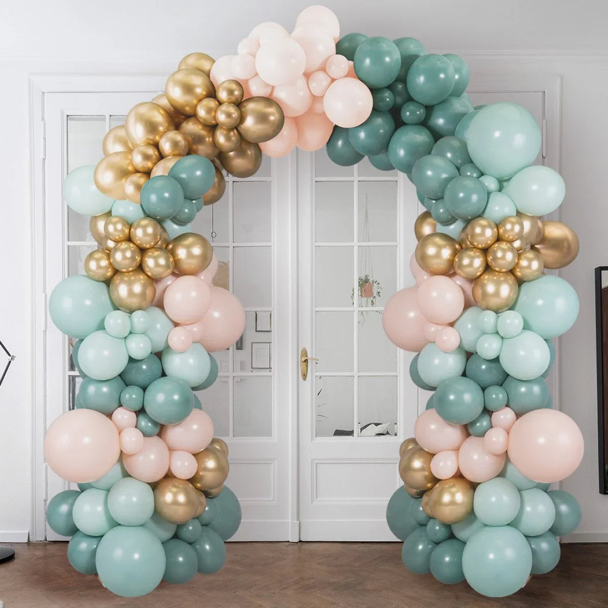 Elegant balloon arch in sage green, gold, and blush pink in a modern white room