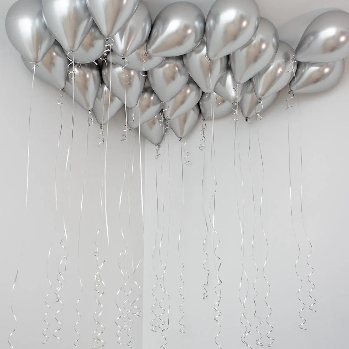 Cluster of shiny silver chrome helium balloons floating near white ceiling with curly ribbons