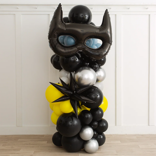 Batman-themed balloon pillar with black mask balloon, black, yellow, silver clusters on wooden floor