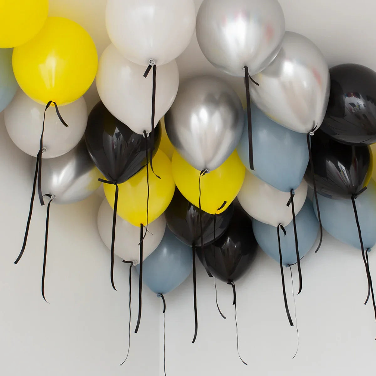 Helium balloons in yellow, black, silver, white, and blue floating near a white ceiling