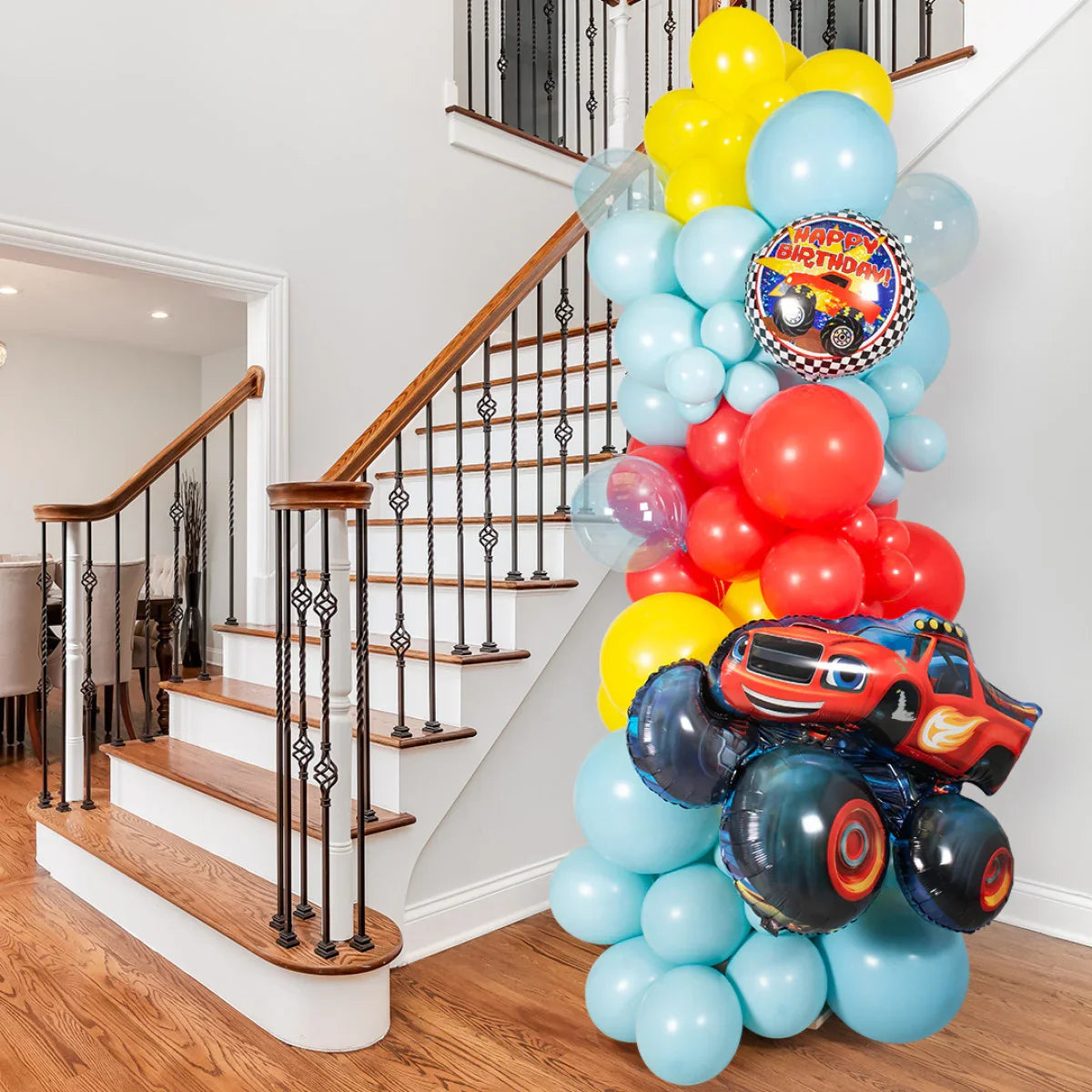 Colorful birthday balloon pillar with Blaze monster truck design next to wooden staircase indoors