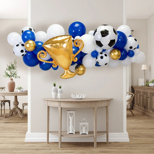 Blue, white, gold, and soccer ball foil balloon garland with large gold trophy balloon in a modern room