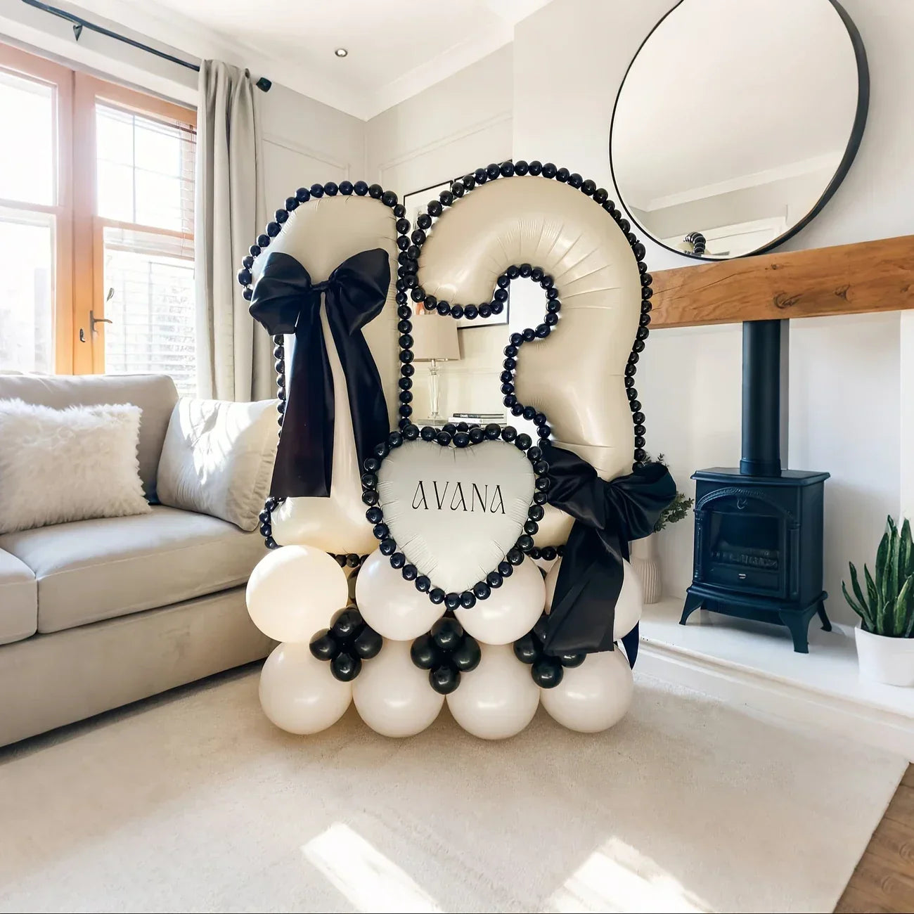 White balloon arrangement shaped as number 13 with black trim, bows, and heart balloon reading AVANA in a modern living room