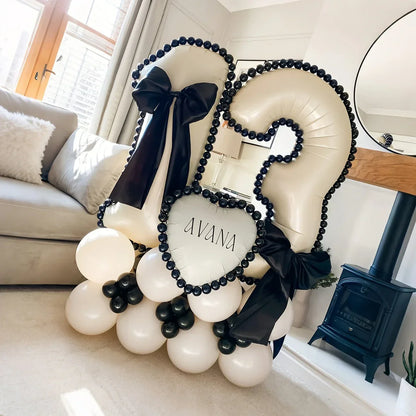 White number 12 balloon arrangement with black bows and black bead trim on beige balloons in living room