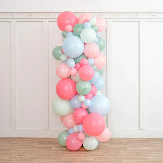 Colorful balloon pillar with pink, blue, green, and white balloons against white wall and wooden floor