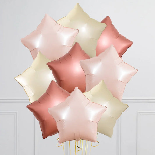 Cluster of metallic star-shaped foil balloons in soft pink, rose gold, and cream colors against white wall