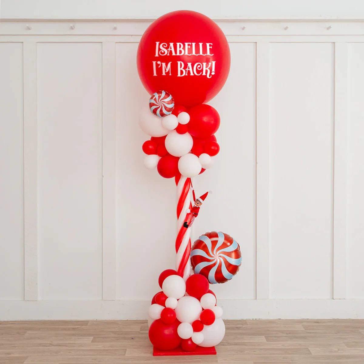 Red and white Christmas balloon pillar with text Isabelle I'm Back and Elf on the Shelf decoration
