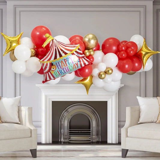 Red, white, gold balloon garland with circus tent happy birthday balloon above white fireplace in elegant living room