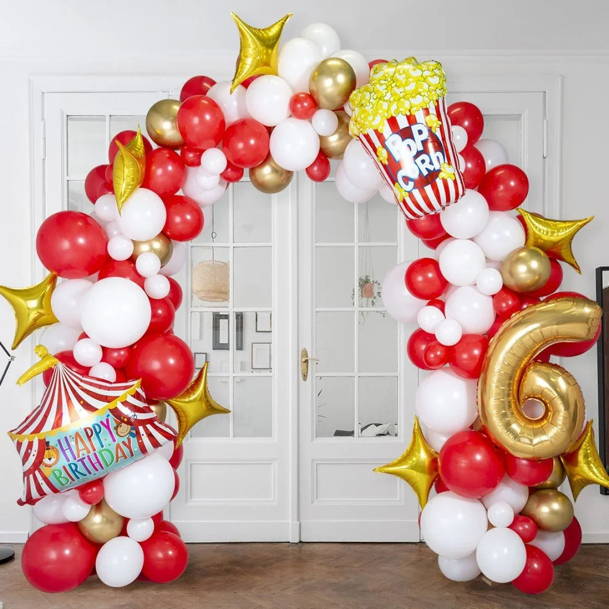 Colorful circus-themed balloon arch with red, white, gold balloons, star shapes, popcorn and happy birthday decor