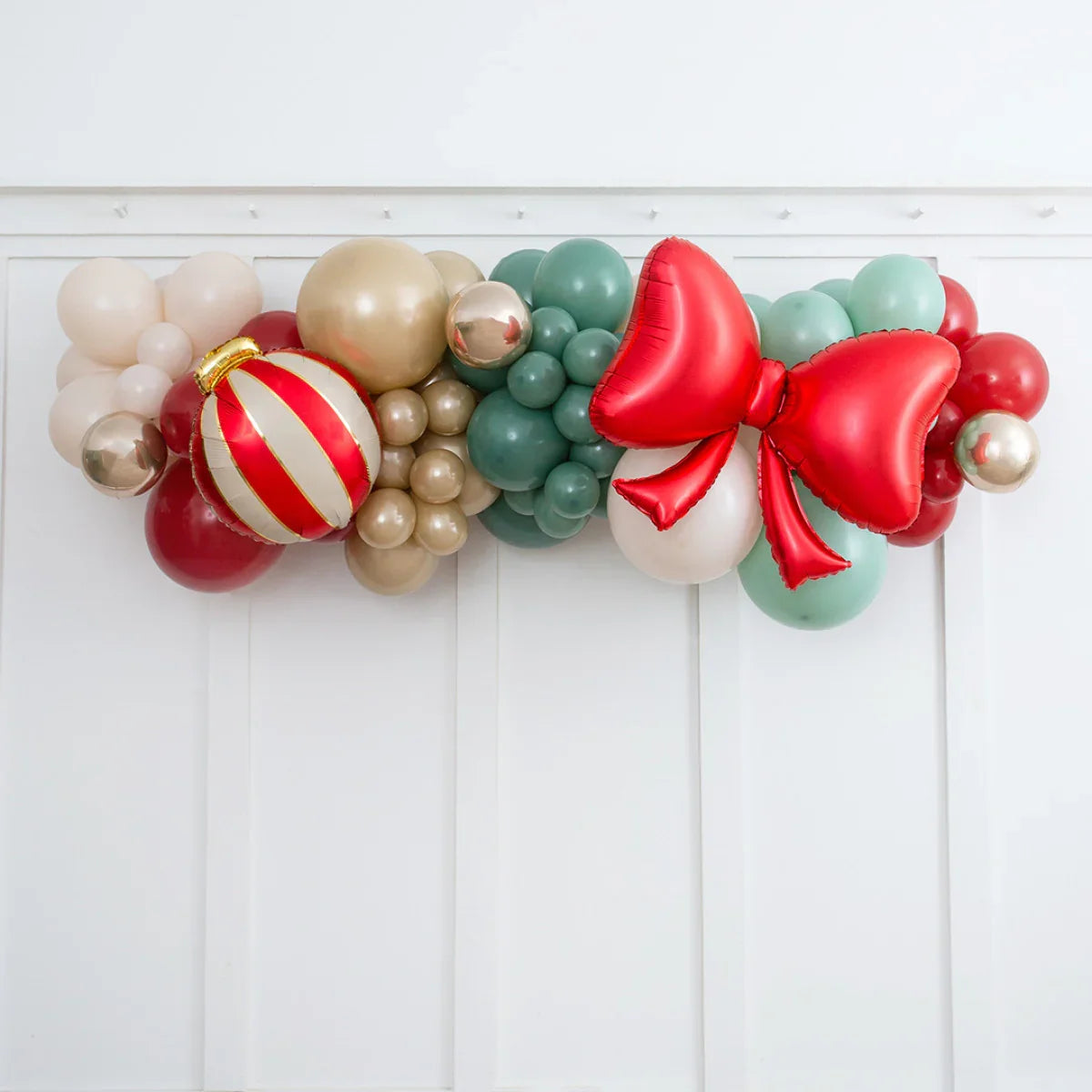Christmas balloon garland with red, gold, green balloons and a large red bow on white wall
