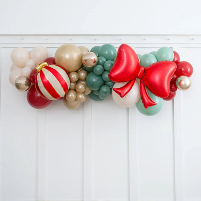 Christmas balloon garland with red, gold, green balloons and a large red bow on white wall