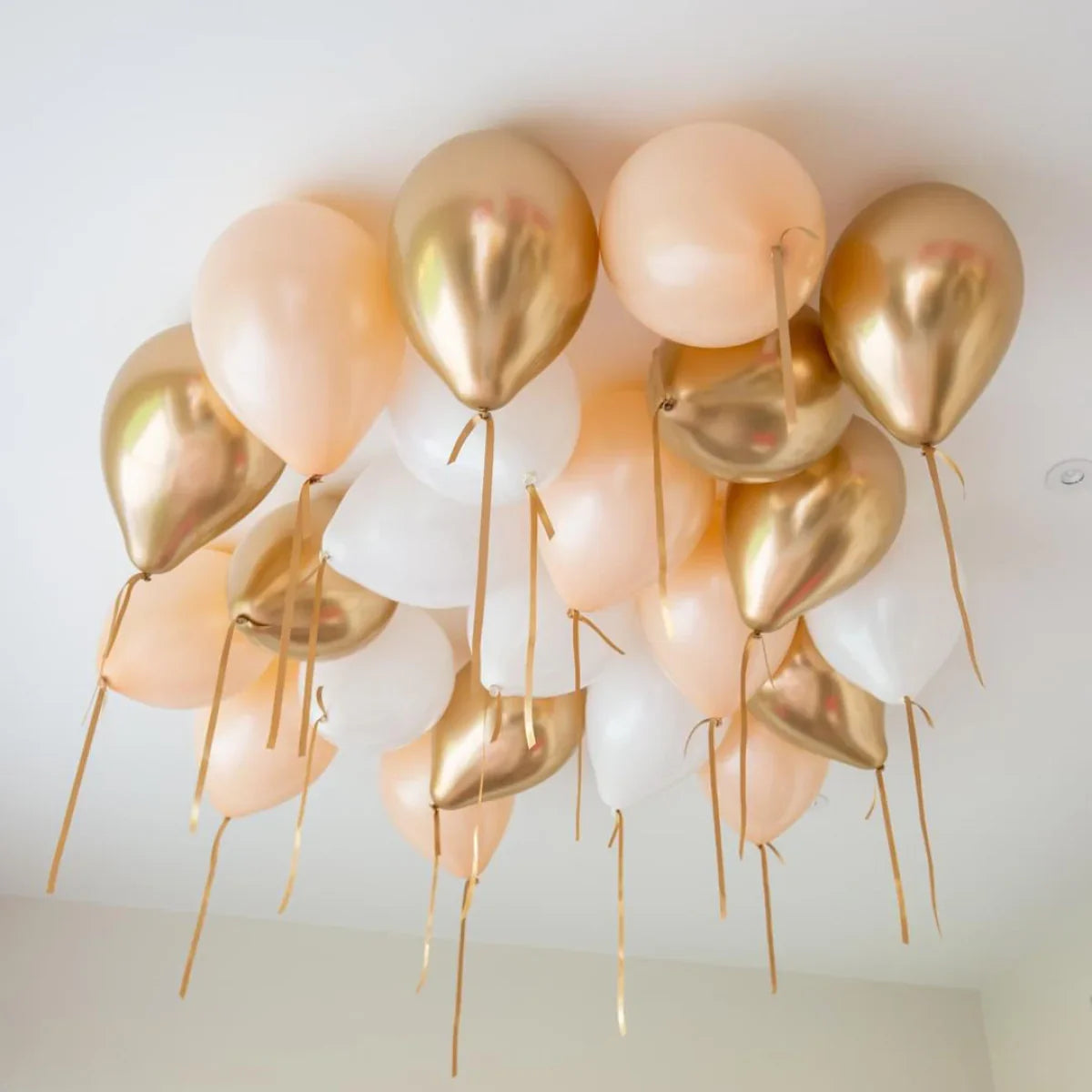 Cluster of cream, chrome gold, and white helium balloons floating on a ceiling with gold ribbons