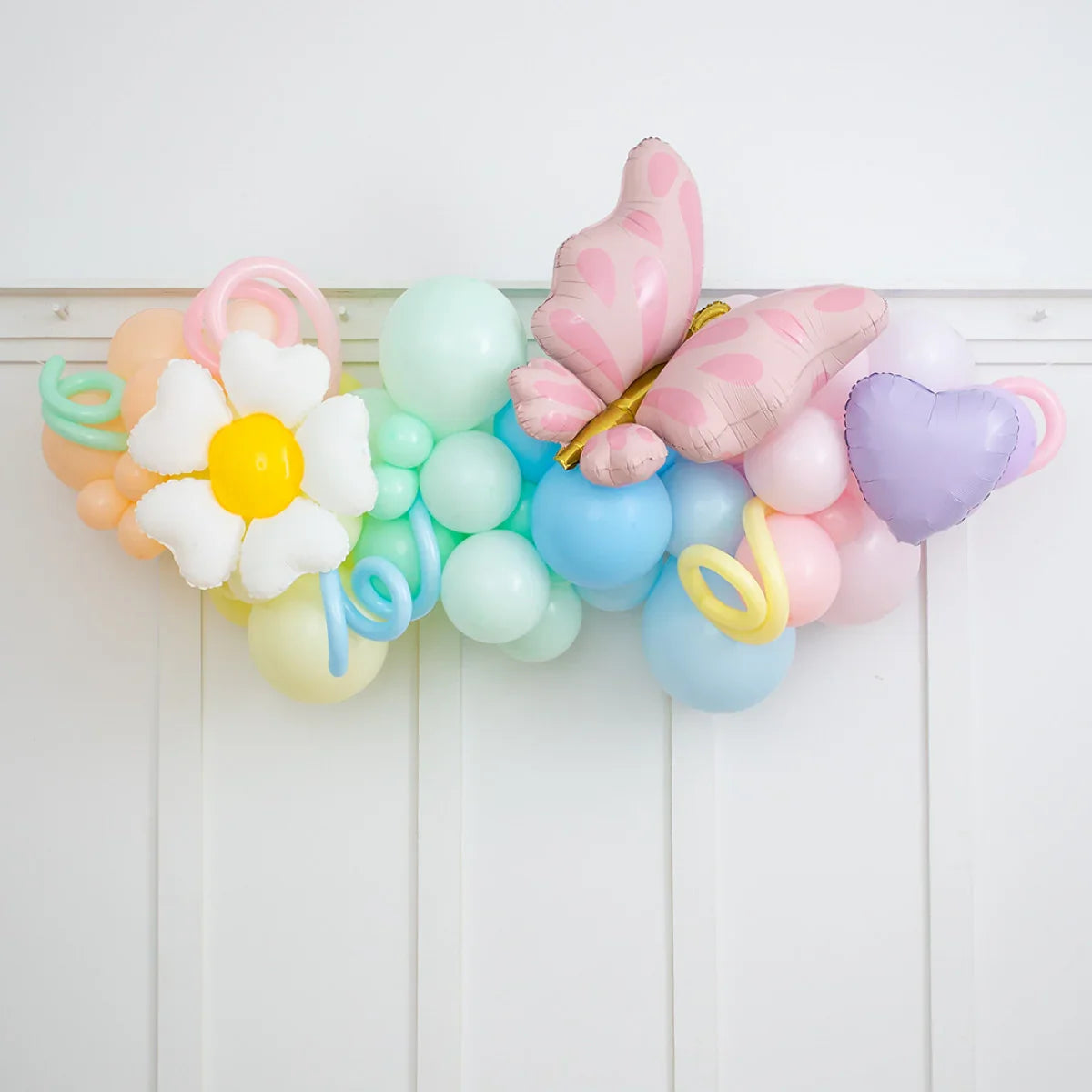 Pastel balloon garland with daisy, pink butterfly, and purple heart balloons on white wall