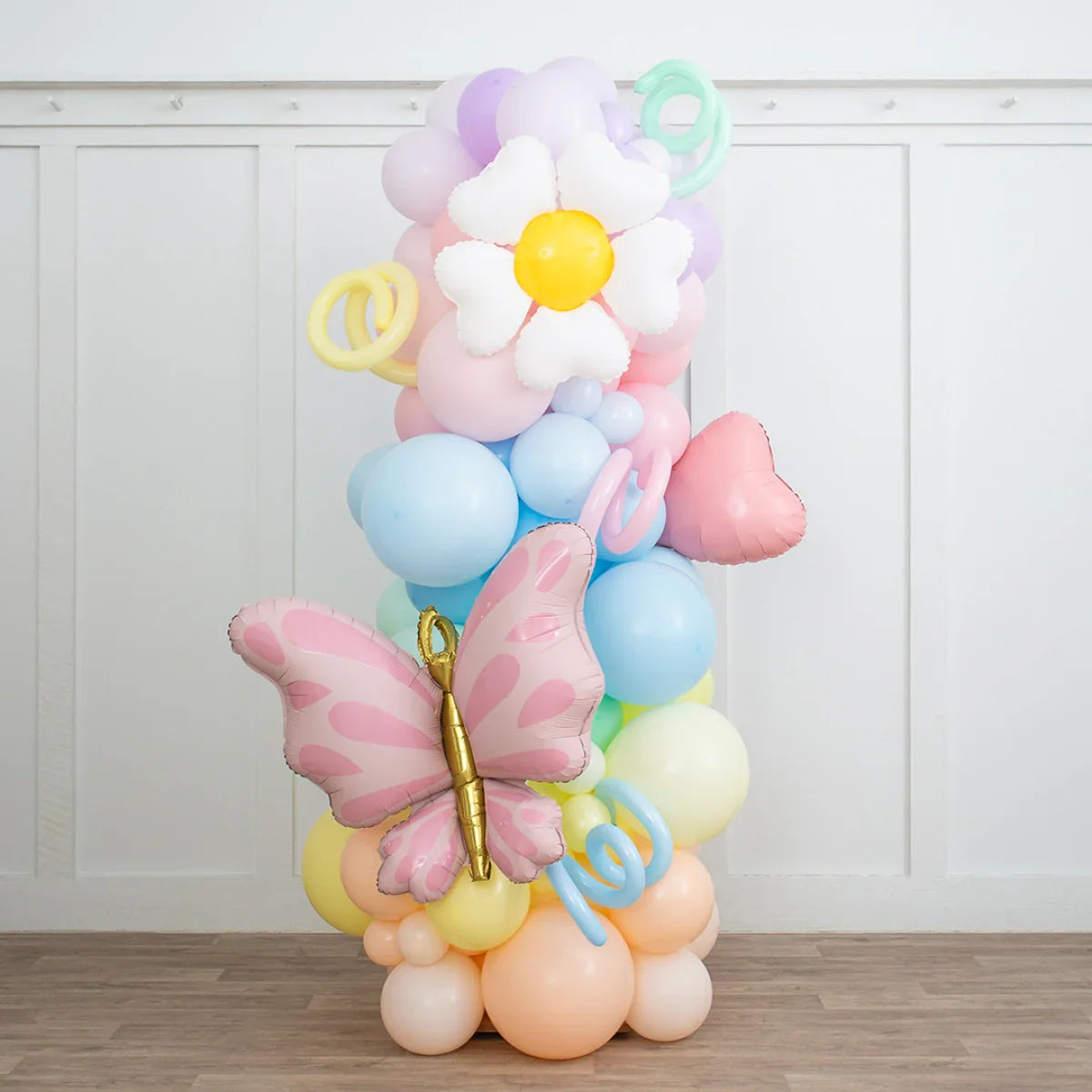 Pastel rainbow balloon pillar with white daisy, pink heart, and butterfly foil balloons