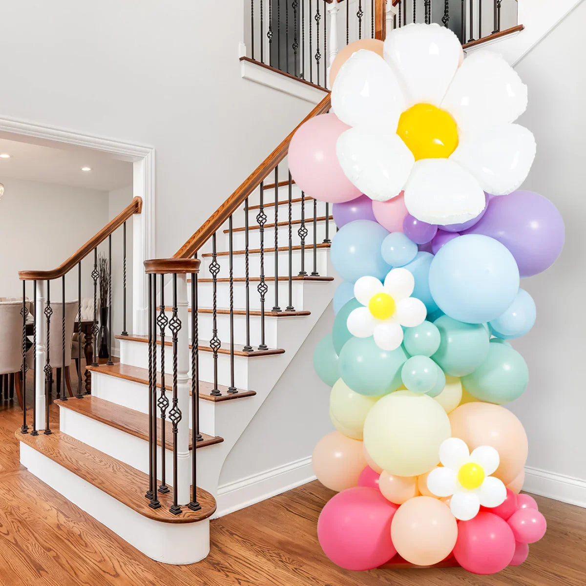 Colorful pastel balloon pillar with white daisy balloons near wooden staircase in modern home