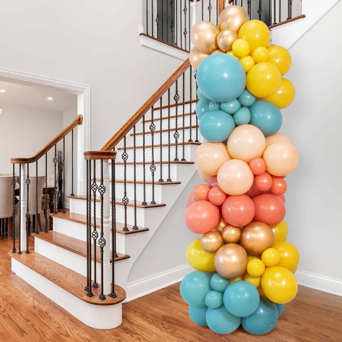 Colorful balloon pillar decoration with yellow, blue, peach, coral, and gold balloons next to wooden staircase