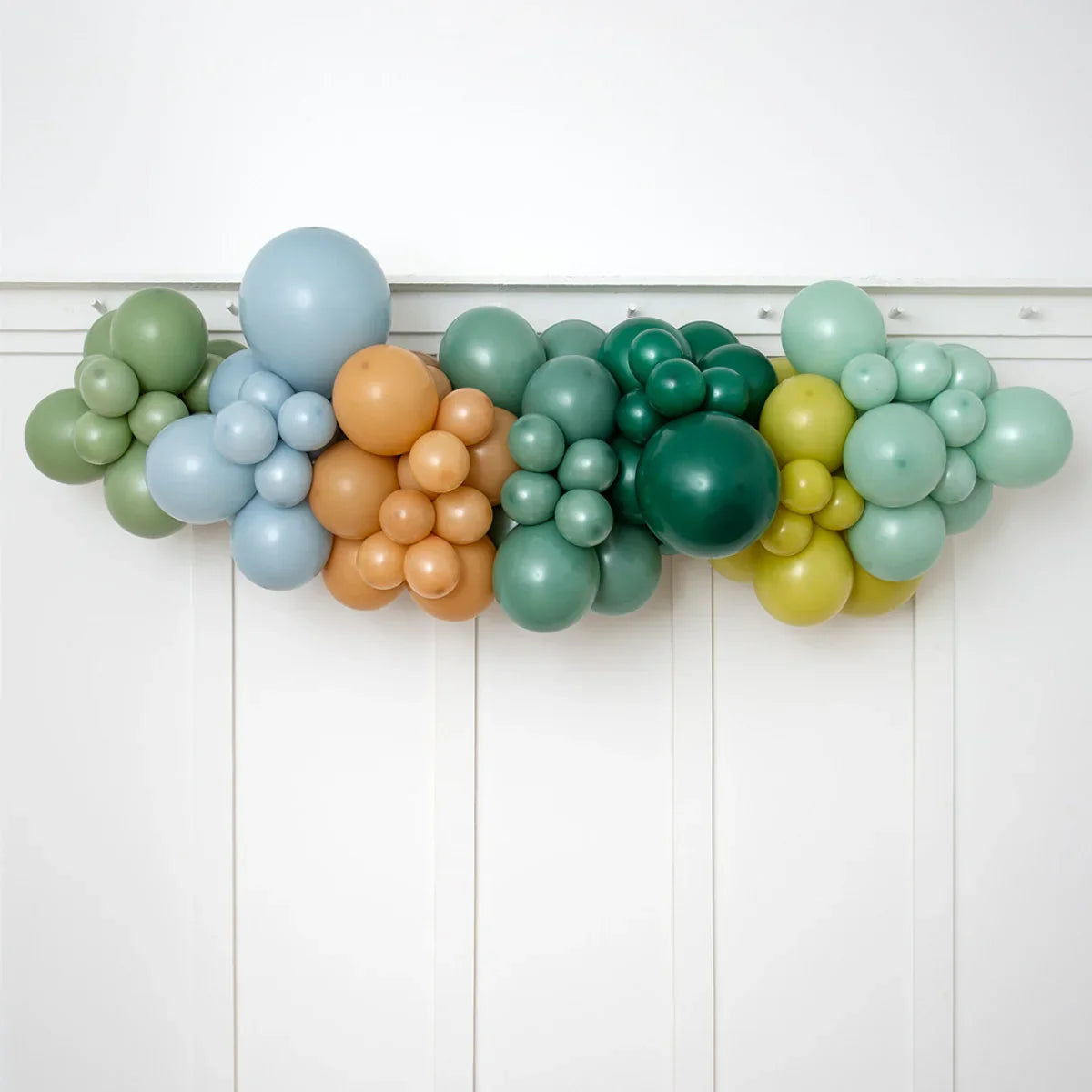 Colorful balloon garland in pastel green, blue, brown, and yellow shades decorating white wall