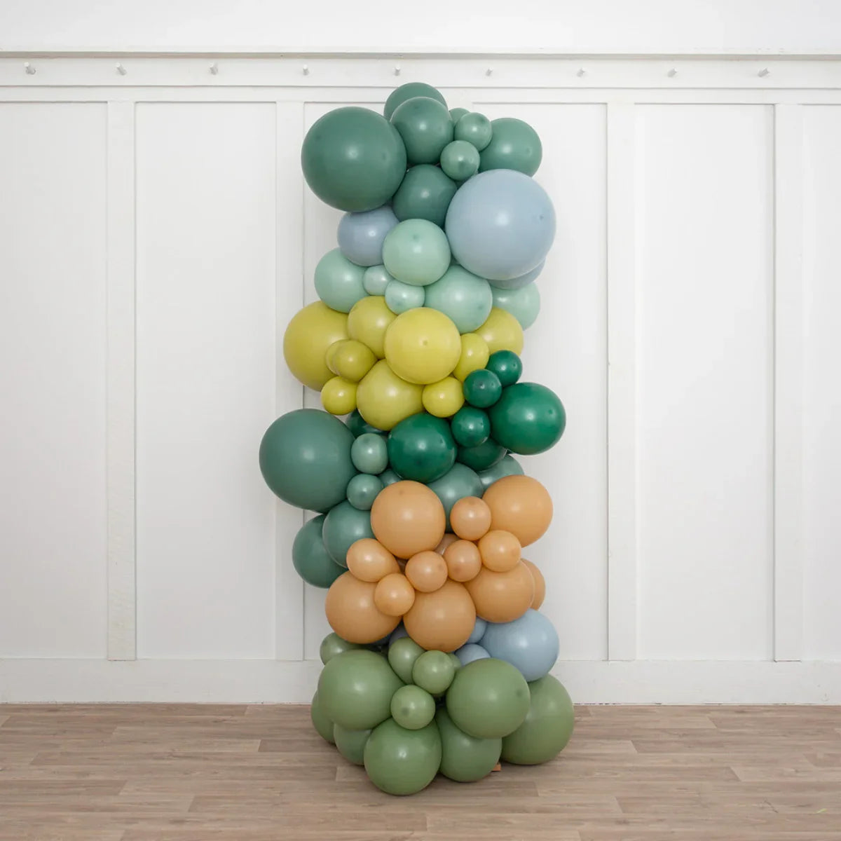 Tall balloon pillar with green, blue, yellow, and orange balloons in a white room with wood floor