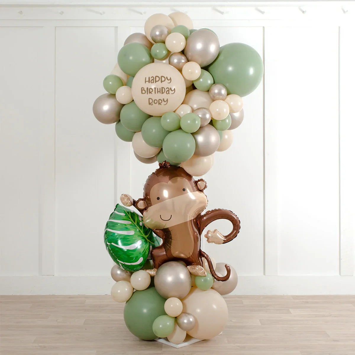 Birthday balloon arrangement with green, cream, and silver balloons and a monkey foil balloon holding a green leaf