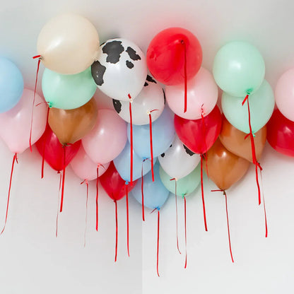 Helium balloons with red ribbons floating on a white ceiling, including cow print and pastel colors