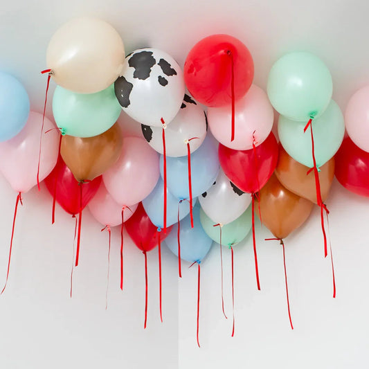 Helium balloons with red ribbons floating on a white ceiling, including cow print and pastel colors