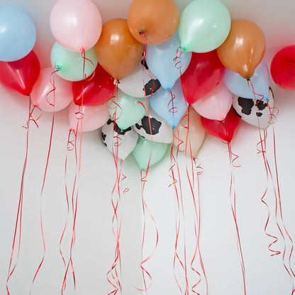 Colorful helium balloons with red ribbons floating on the ceiling, including cow print and pastel colors