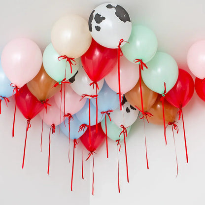 Colorful helium farmyard balloons with red ribbons floating near white ceiling