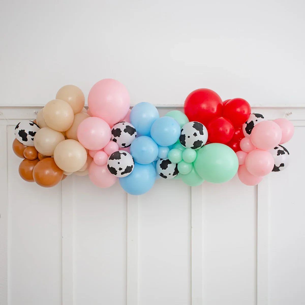 Colorful balloon garland with beige, pink, blue, green, red, and cow-print balloons on a white wall