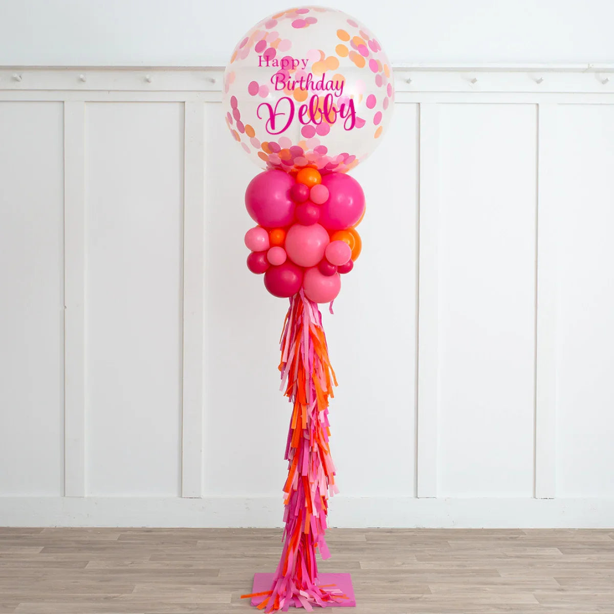 Tall birthday balloon pillar with pink, orange, and red balloons and confetti balloon saying Happy Birthday Debby