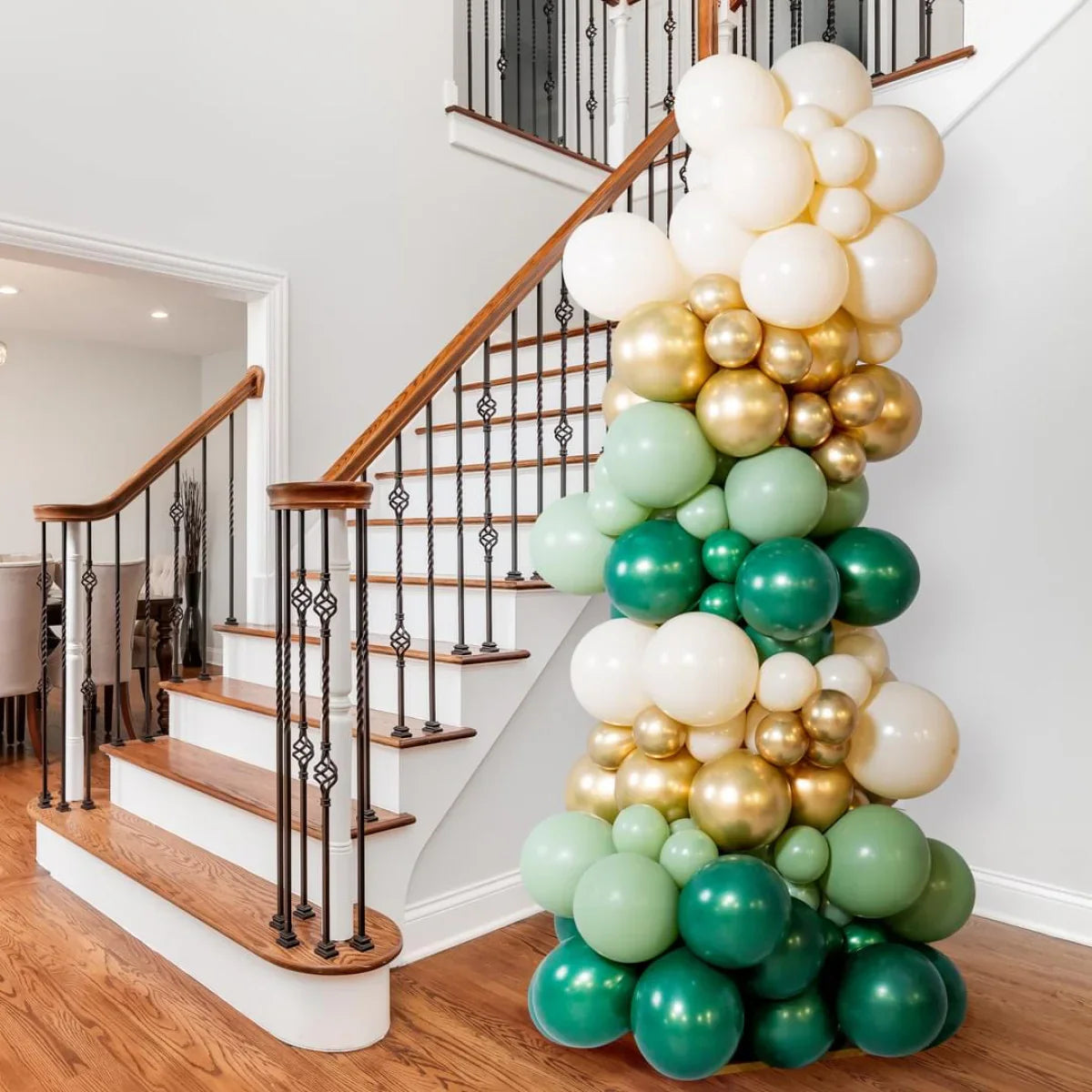 Balloon pillar with green, gold, and white balloons next to wooden staircase with black iron railing
