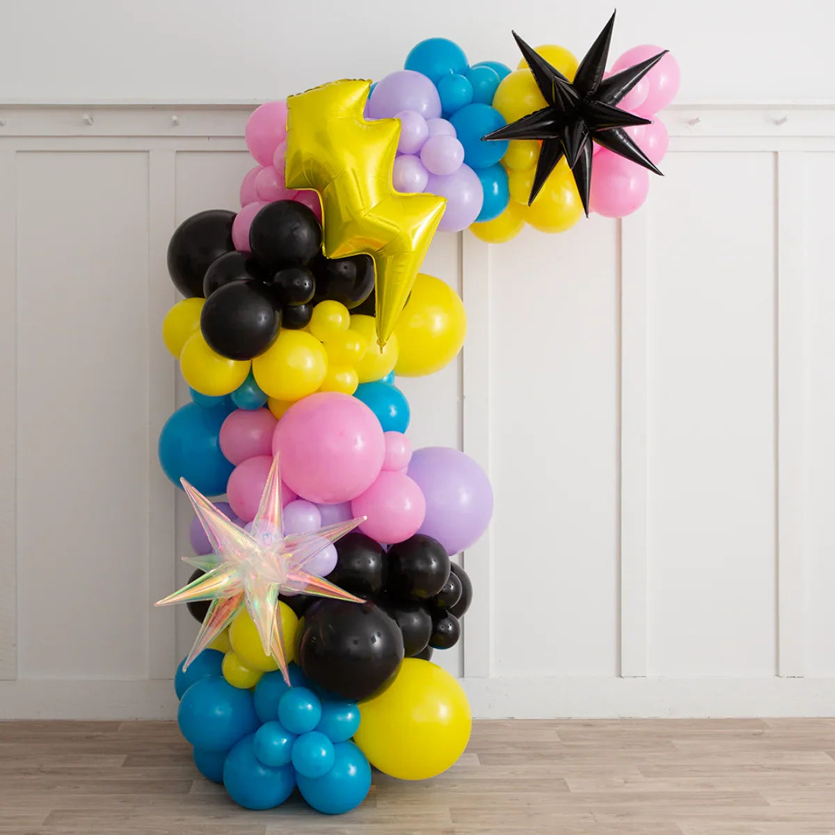 Colorful asymmetric balloon arch with yellow lightning bolt, black stars, and pastel balloons in indoor setting