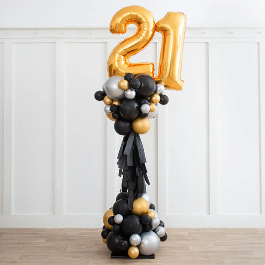 Tall balloon decoration with gold foil number 21 and black, gold, silver balloons on stand