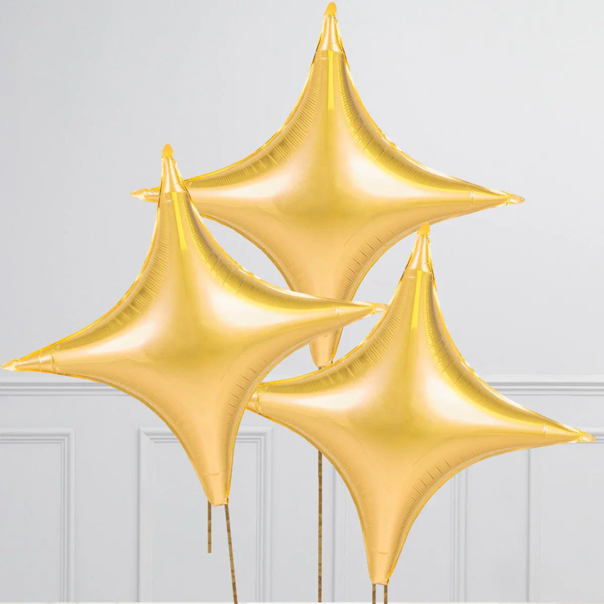 Trio of shiny gold star-shaped foil balloons against a white paneled wall
