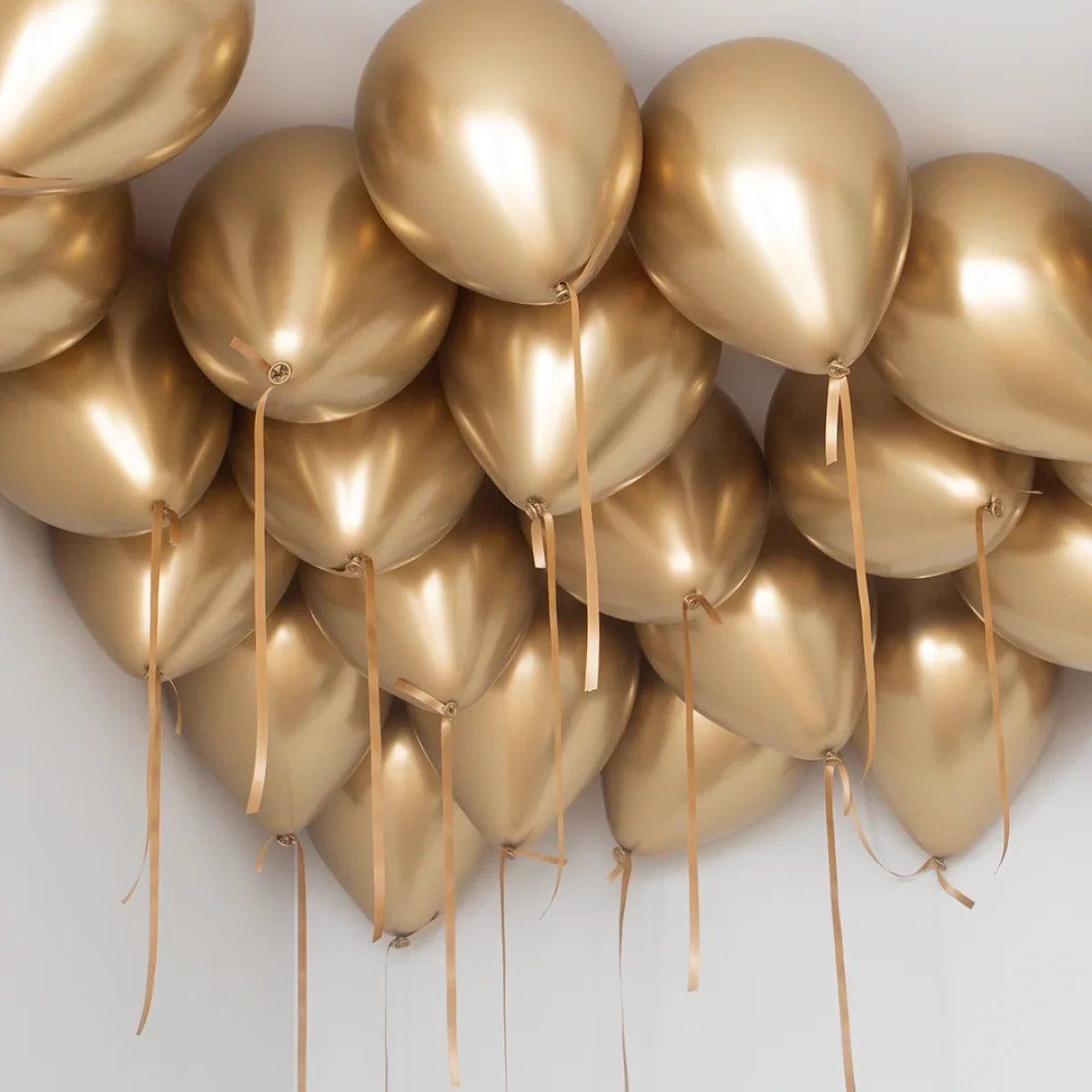 Cluster of shiny gold helium balloons attached to ceiling with gold ribbons