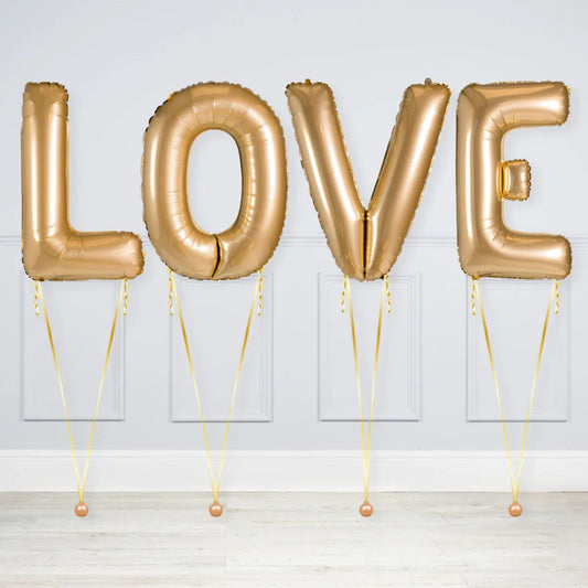 Gold foil balloons spelling LOVE with ribbon weights in a white room with panel walls