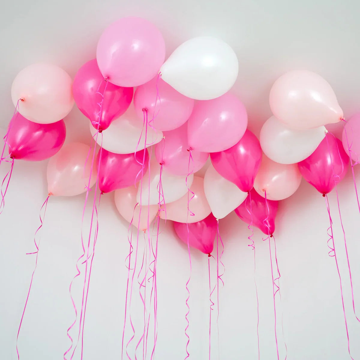 Cluster of pink, white, and light pink helium balloons floating near white ceiling with ribbons