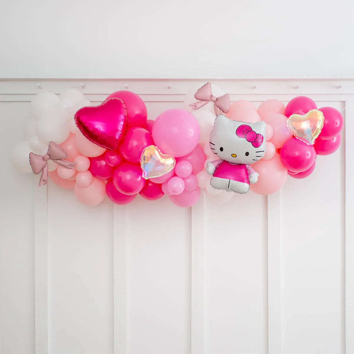 Hello Kitty pink balloon garland with heart-shaped and bow-shaped balloons on white wall