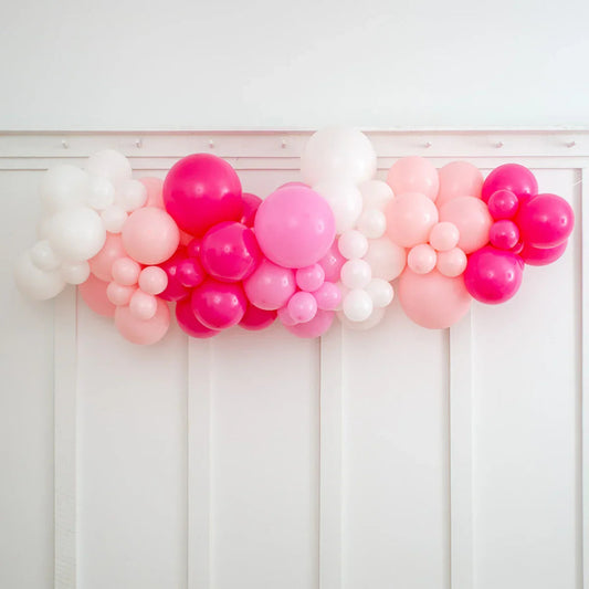 Pink, white, and red balloon garland decoration hanging on white paneled wall