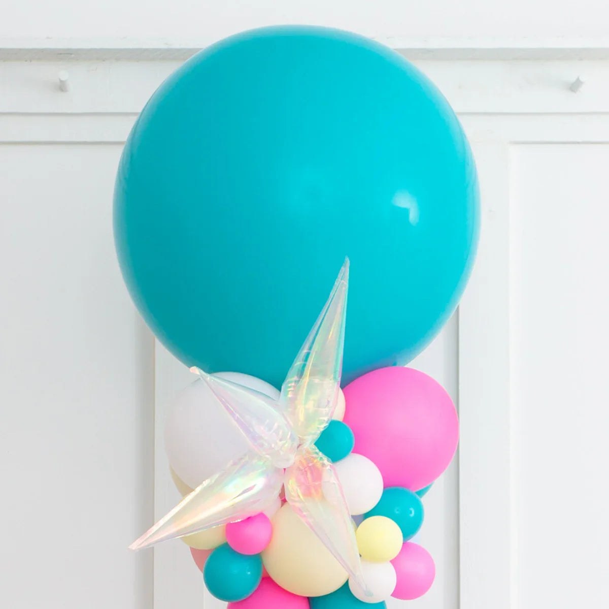 Colorful balloon pillar with large teal balloon and iridescent star decoration on white wall