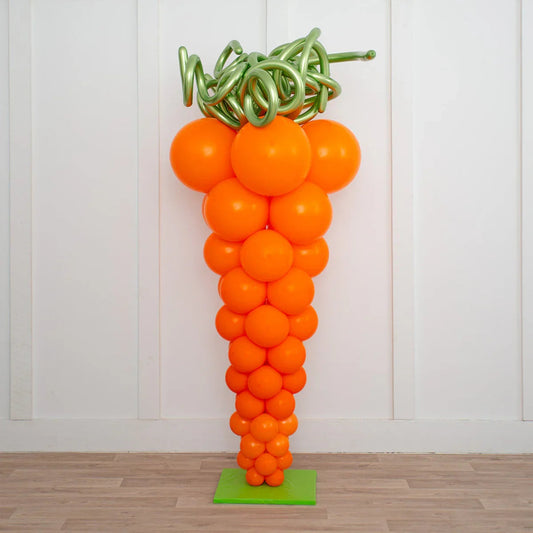 Large orange balloon pillar shaped like a carrot with green curly balloon top on green base