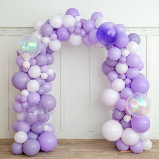 Lavender and white balloon arch with iridescent and purple balloons on wooden floor and white wall