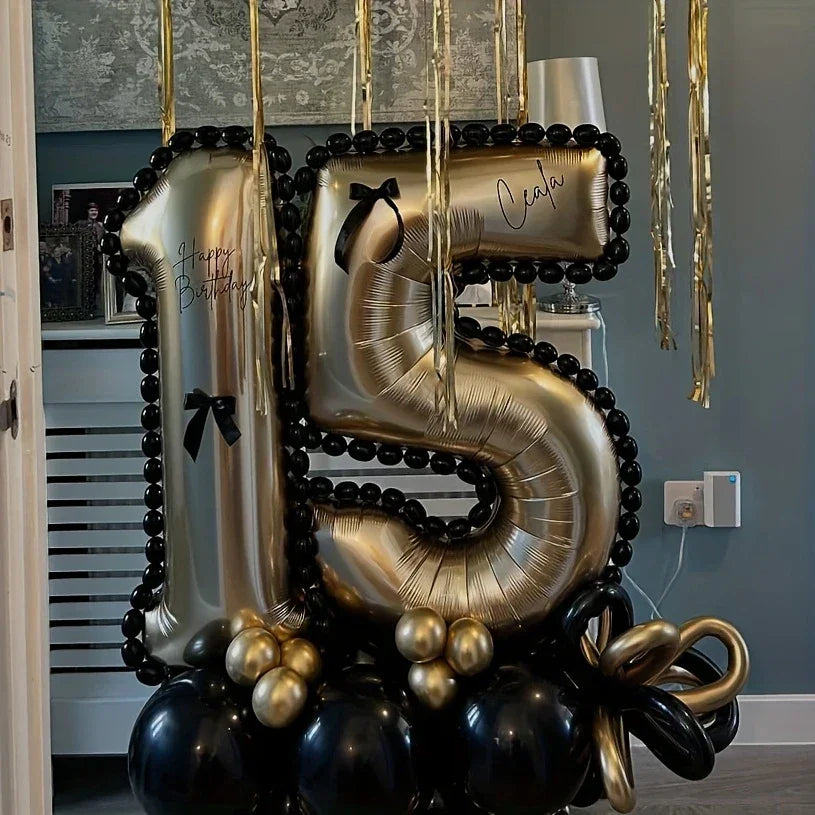 Gold number 15 birthday balloons decorated with black balloons and gold hanging streamers in a modern room