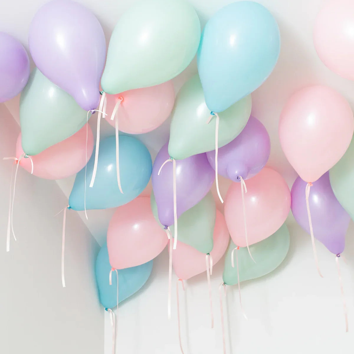 Pastel helium balloons in pink, blue, green, and purple floating against a white ceiling