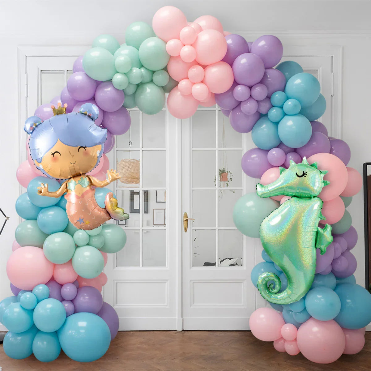Pastel balloon arch with mermaid and seahorse foil balloons in front of white double doors