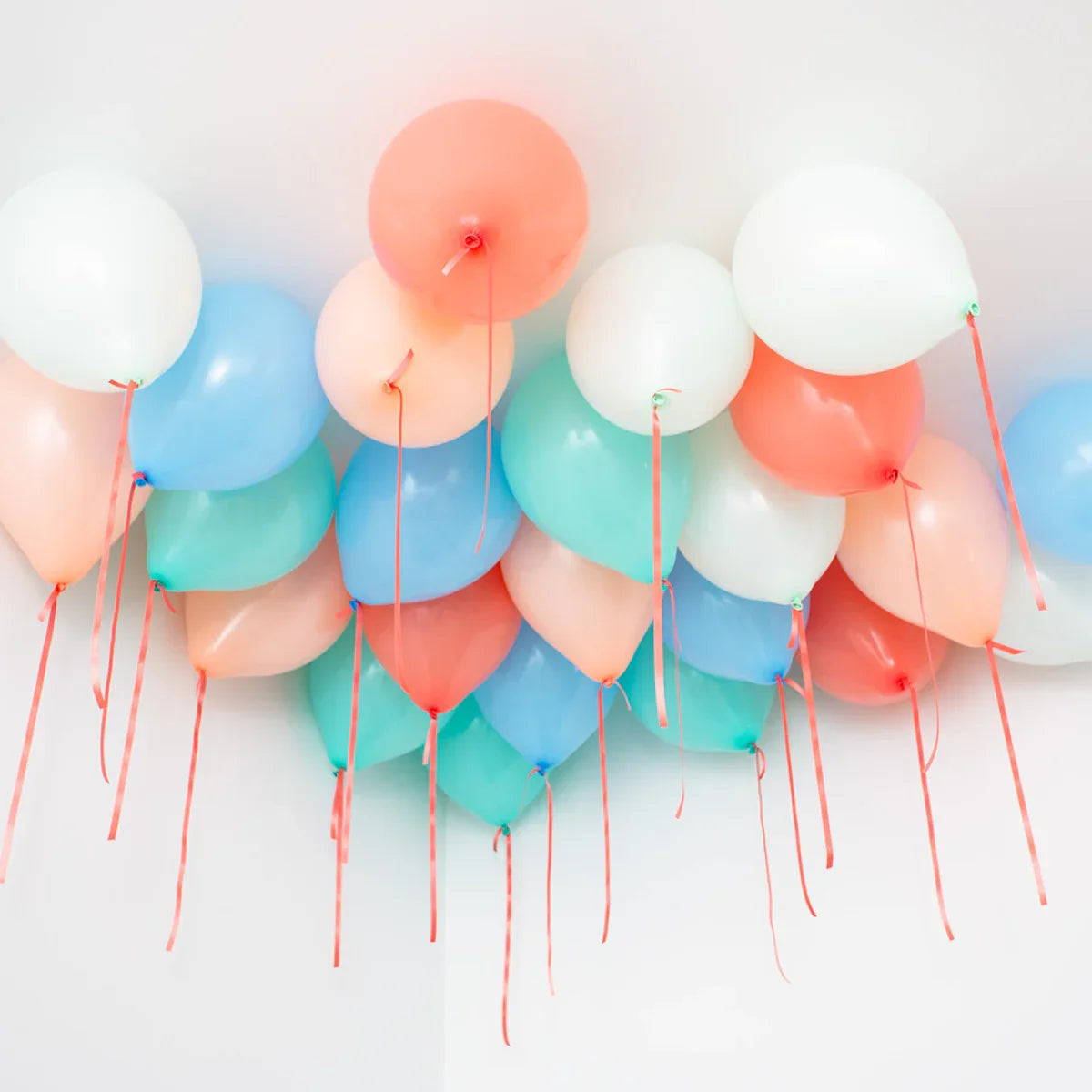 Colorful helium balloons in pastel shades of blue, white, pink, and green floating on a white ceiling